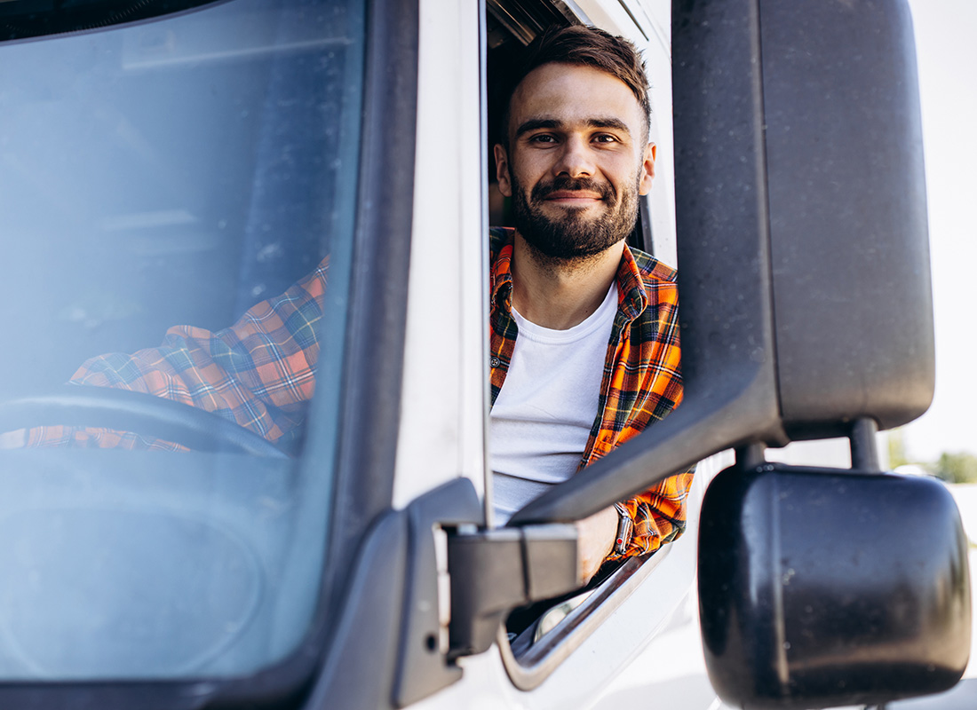 Contact - Young Smiling Truck Driver Wearing a Plaid Shirt Driving a White Truck While Looking Out the Window