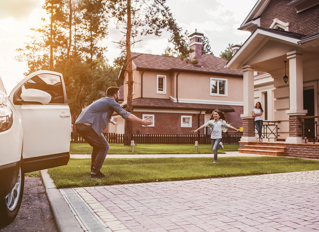 Insurance Solutions - Excited Young Girl Running Through the Green Grass in Front of a House to her Father Standing Next to a Car with Open Arms
